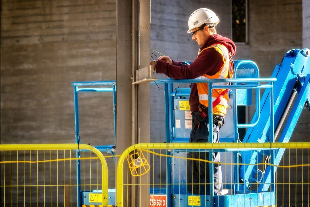 Electrician in a hard hat and safety vest fixing wiring from a lift