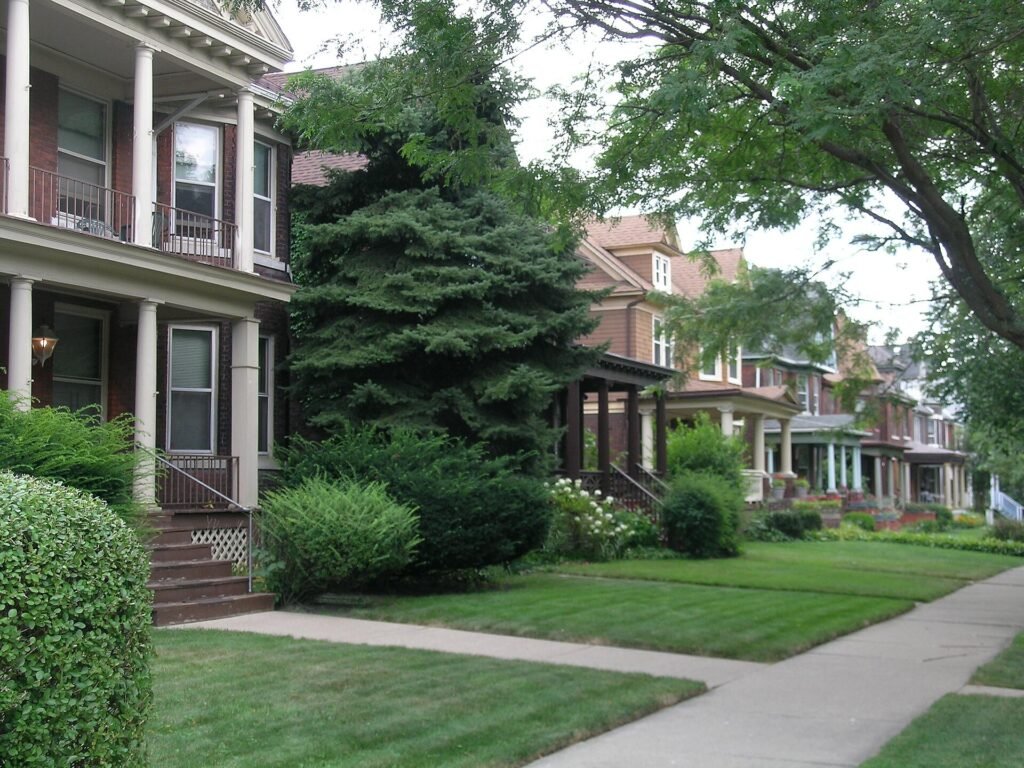 Row of older brick and frame houses with porches on a tree-lined Detroit street