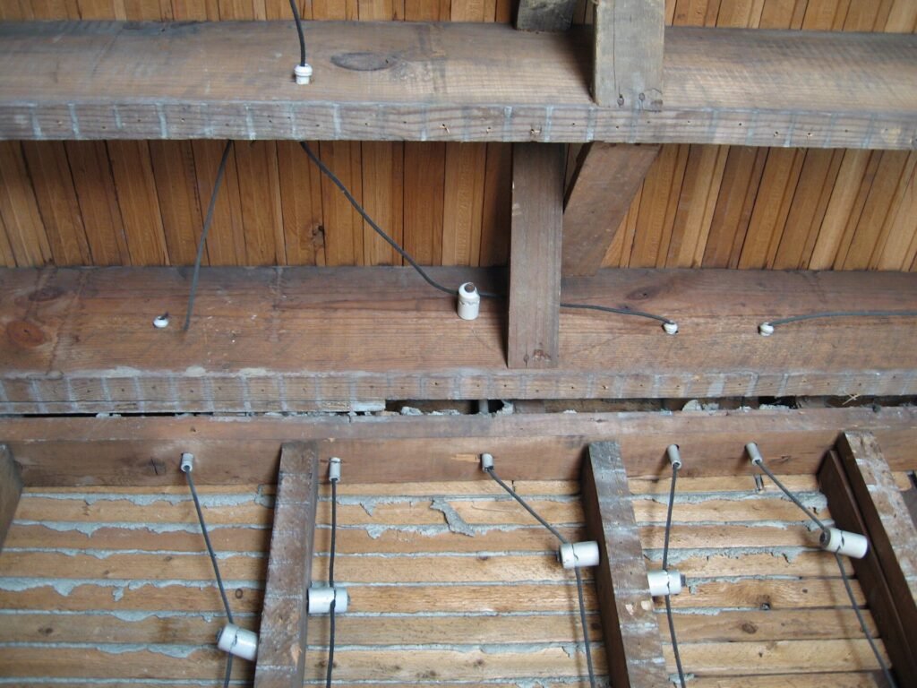Knob-and-tube wiring with porcelain insulators running across wooden joists in older house