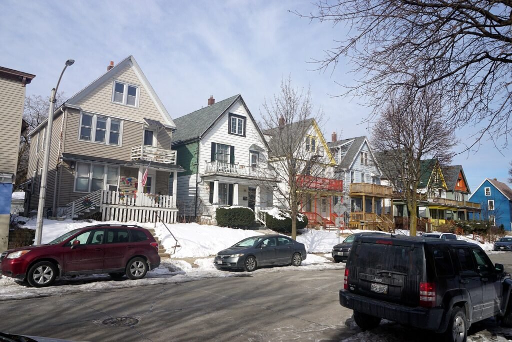 Older frame houses and parked cars on a snowy Milwaukee street in winter